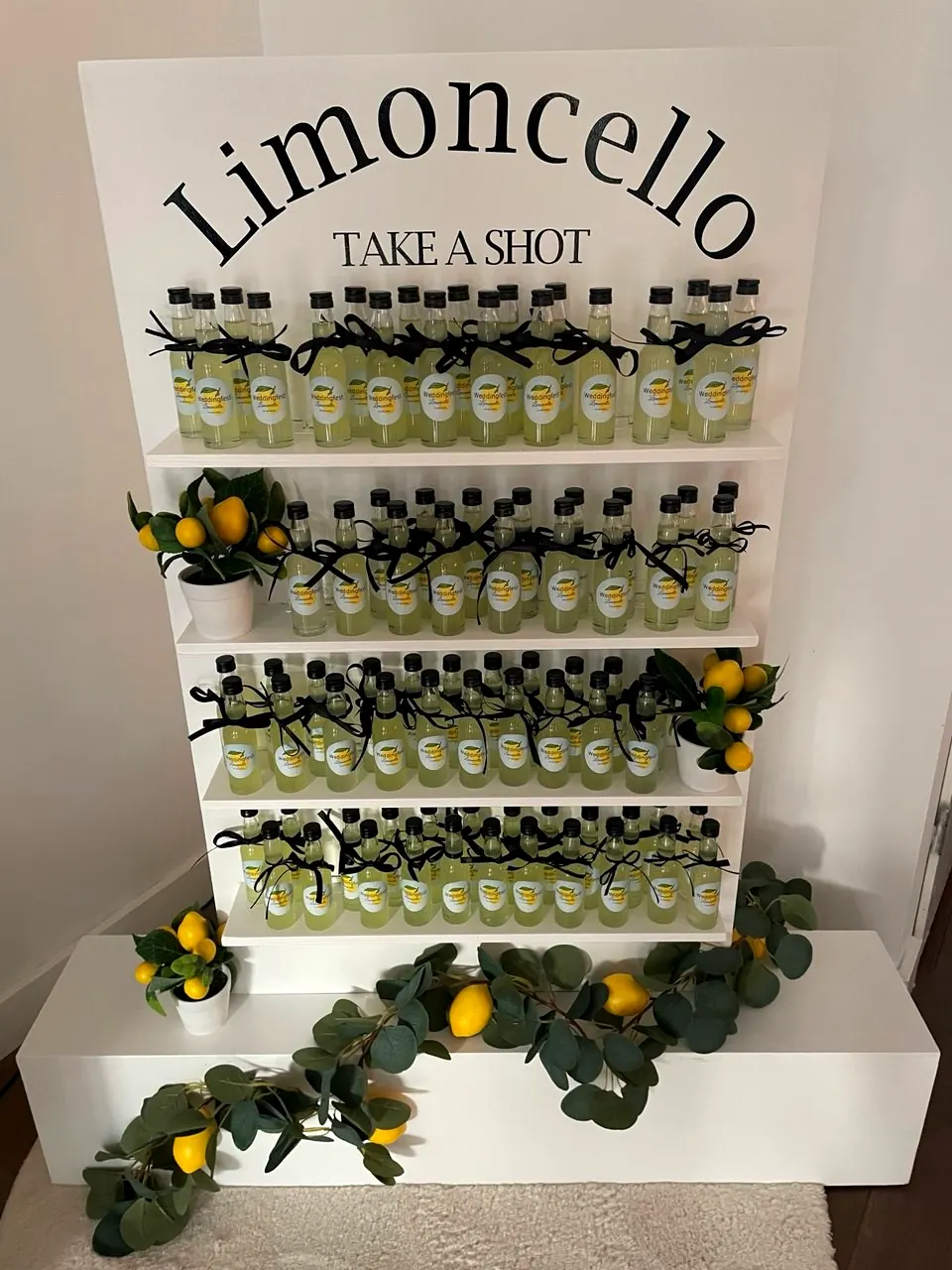 Limoncello Wall met mini-flesjes limoncello, zwarte strikjes, citroenen en eucalyptus